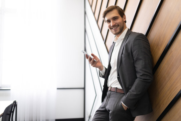 年轻的男性商人，穿着西装，手里拿着手机，背景上的办公室价格图片下载
