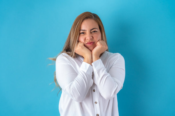 美丽迷人的年轻女商人摆出愤怒的痛苦在她的脸上，在白色衬衫和灰色裤子。在蓝色背景上隔离。图片下载