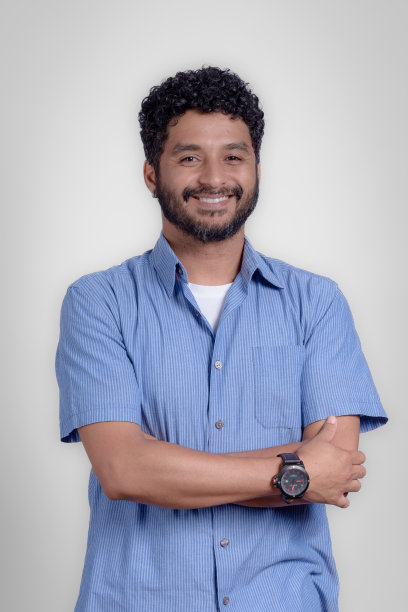 年轻男子的肖像与双臂交叉微笑，看着相机在工作室与灰色背景图片下载