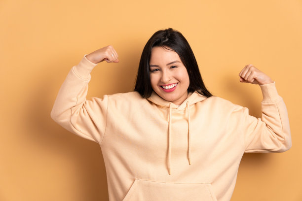 有趣的年轻女子在米色背景弯曲手臂。强，力，傲的理念。图片下载