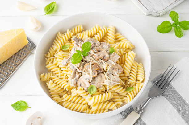 蘑菇、奶酪和新鲜罗勒的Fusilli意大利面，放在白色木制背景的盘子里。图片下载