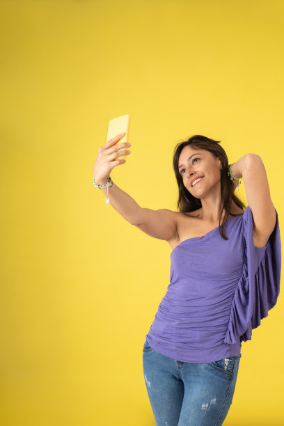 年轻女子微笑着用她的黄色手机自拍图片下载