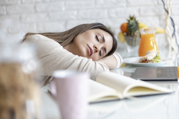 疲惫的年轻女子和书睡在家里的桌子上图片下载