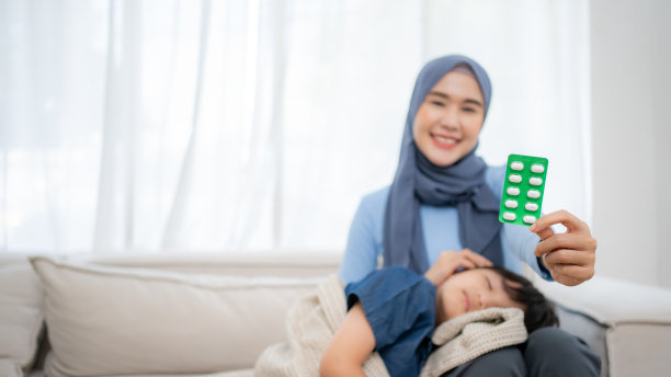 关怀的亚洲母亲抱着生病的儿子额头的特写照片。展示一个药包。图片下载