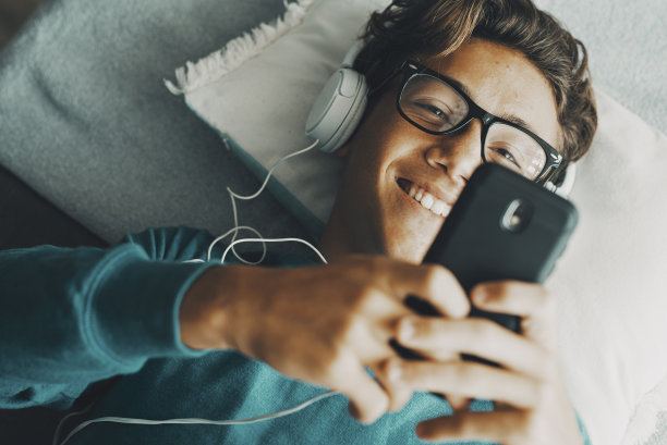 快乐的小男孩使用手机应用程序听音乐耳机。现代人用手机在网上聊天约会。上图是学生享受上网上网活动的景象图片下载