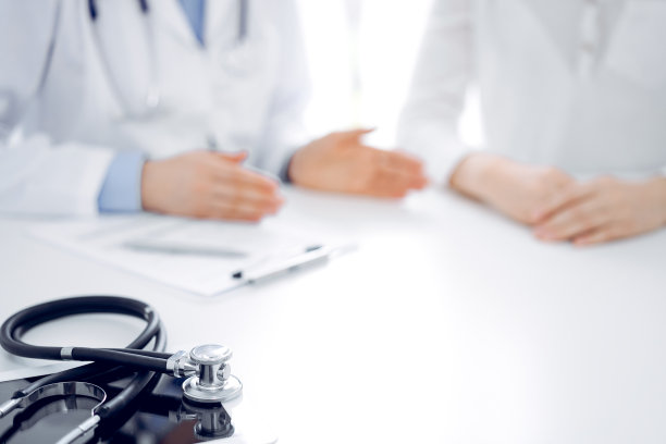 听诊器放在平板电脑上，医生和病人坐在一起。医学、保健概念图片下载