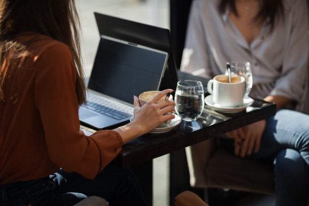 两个年轻的女商人在咖啡馆里一对一地开会。朋友们下班后聊八卦，坐在靠窗的桌子边喝咖啡。图片下载