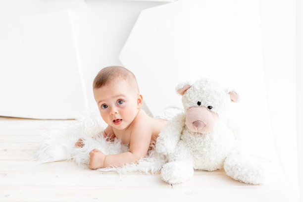 一个6个月大的小女孩穿着尿布躺在明亮的公寓里，和一只柔软的熊在一起图片下载