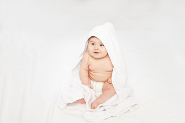 宝宝沐浴后裹着毛巾坐在白色垫子上图片下载