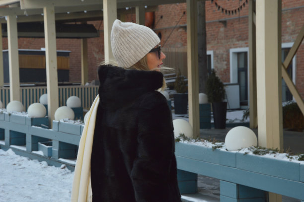 一个女孩的城市肖像。在寒冷的天气里，一名戴着白色帽子、毛皮大衣和太阳镜的时尚年轻女子在户外摆拍。图片下载