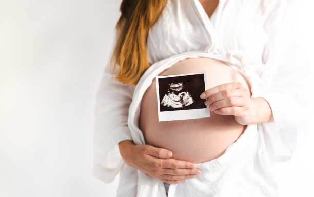 不认识的孕妇摸着肚子站在白色的墙上，拿着超声波照片。复制空间，生活方式，极简主义理念图片下载