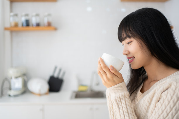 年轻亚洲女人身穿毛衣在家中厨房喝茶图片下载