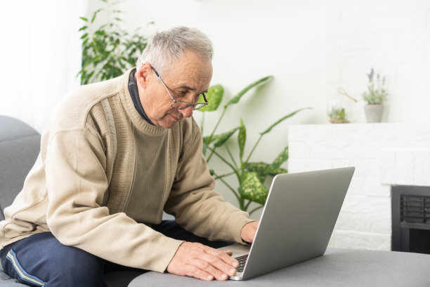 老人戴着眼镜和笔记本电脑连接在家里。图片下载