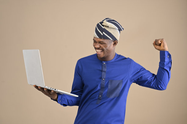 兴奋快乐的非洲人看着笔记本电脑屏幕，庆祝胜利孤立在棕色背景。图片下载