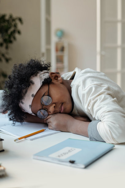 可爱的小学生在书桌前打盹，同时保持头在打开的抄写本上图片下载