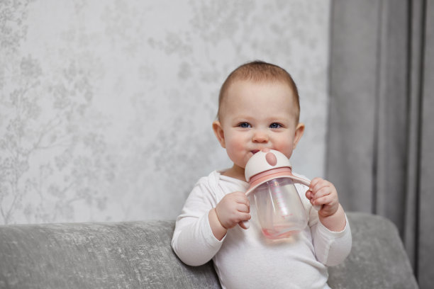 可爱的女婴拿着瓶子喝水。图片下载