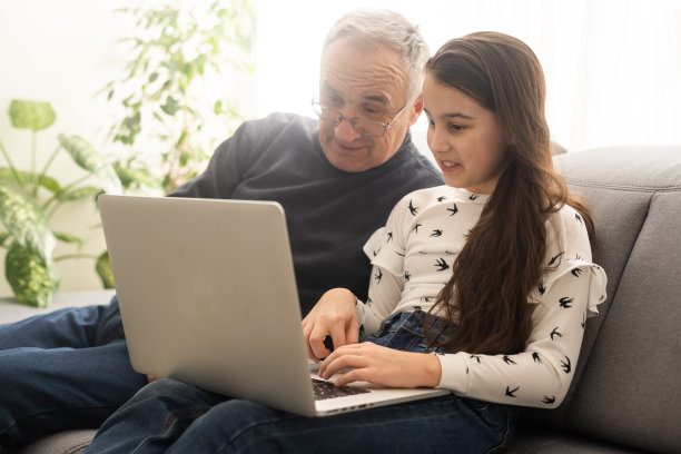 快乐退休的爷爷和漂亮的孙女一起通过笔记本电脑看电子书学习教育。居家教育理念。科技和教育。图片下载