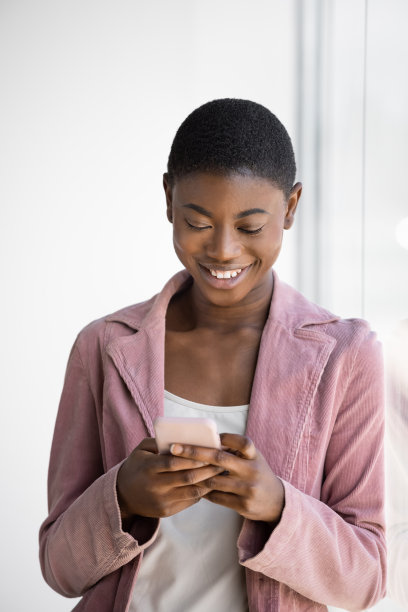 微笑的黑人妇女靠在玻璃窗上用智能手机发短信图片下载