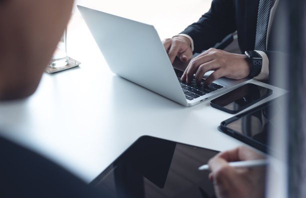 身着黑色西装的商人和他的同事坐在桌子旁，在笔记本电脑和平板电脑上工作，在现代办公室，商务会议，团队合作理念，近距离观察图片下载