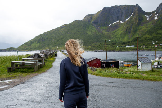 一个女人看着一个小镇。探索挪威。北方风景优美。海洋和山脉。斯堪的纳维亚风格的建筑。享受当下，放松。旅行、冒险、生活方式图片下载