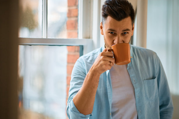 快乐的男人在家里享受一杯咖啡，看着相机。图片下载