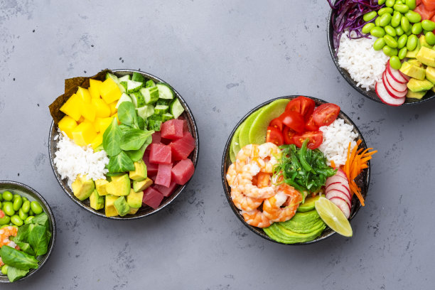 用金枪鱼、三文鱼、虾配鳄梨、芒果、萝卜、米饭等食材做成的Poke碗。酱油和芝麻酱。灰色表背景，顶视图图片下载