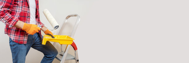 油漆工正在用油漆辊工作，将墙壁涂成灰色。长格式。全景横幅与复制空间。图片下载