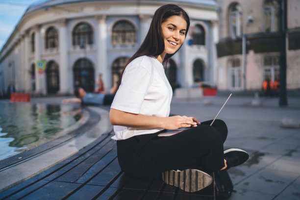 快乐的女性自由职业者的肖像与笔记本电脑微笑在相机享受自由时间在城市，快乐的潮女孩与数字上网本设备做远程工作在城市设置摆姿势图片下载