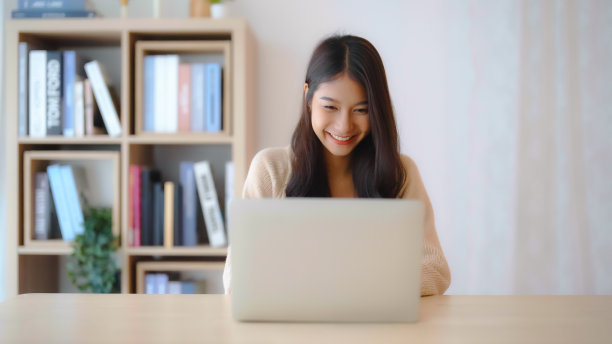 年轻的亚洲女性在家工作。女性在家里的桌子上使用笔记本电脑图片下载