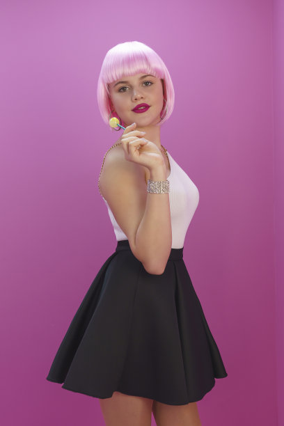 在粉红色背景的玩偶形象中，一个女孩正在顽皮地舔着糖果图片下载