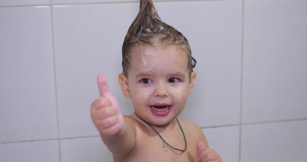 浴室里的小女孩竖起大拇指。小女孩喜欢用洗发水洗头。一个可爱的婴儿沉浸在浴缸里。每天给宝宝洗澡的概念。图片下载