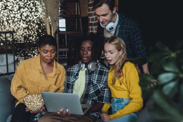 不同群体的大学生、朋友、年轻人一起在笔记本电脑上看电影或电影院，玩得开心，吃着爆米花。国际友谊的概念，闲暇时间，家庭活动图片下载