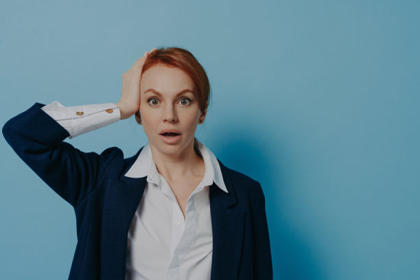 震惊的红头发女办公室职员的肖像，手在头上，下巴掉下来图片下载