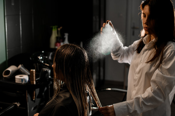 专业美发师将香脂轻柔地洒在女性顾客头发上图片下载