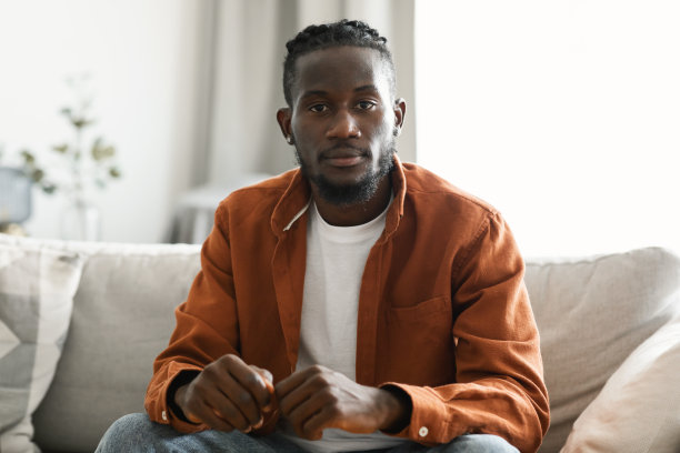 严肃的非裔美国人看着相机的头部照片，坐在家里客厅的沙发上图片下载