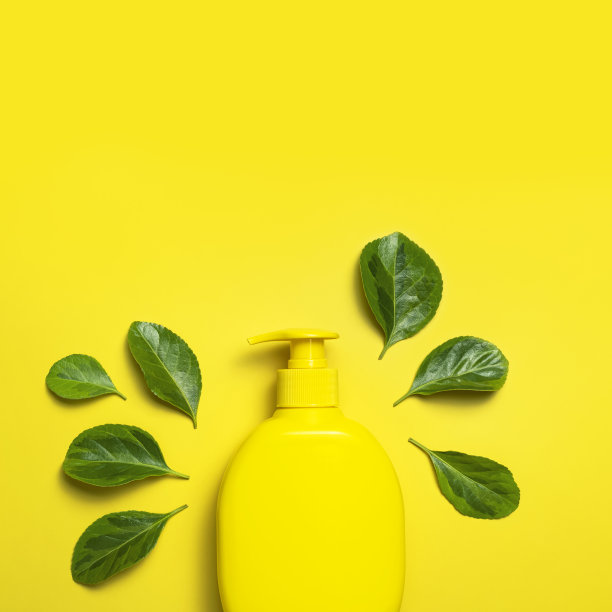 天然有机化妆品。美容，水疗，品牌模型。黄色化妆品瓶容器新鲜的绿叶在黄色背景平铺顶视图。简约的环保化妆品包装概念图片下载