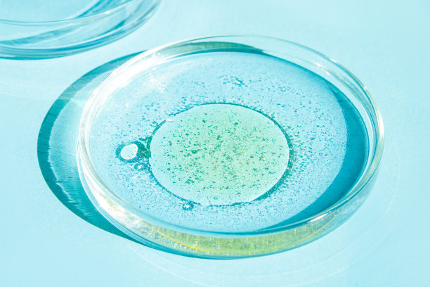 培养皿中。装有液体的皮氏杯。化学元素、油脂、化妆品。凝胶，水，分子，病毒。特写镜头。在蓝色的背景上。图片下载