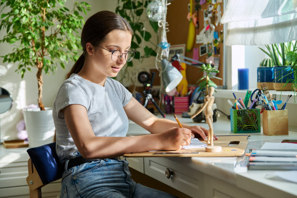 十几岁的女孩坐在家里的桌子前，用铅笔画草图图片下载