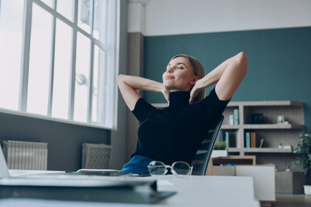 放松的女商人手在头后，坐在她的工作地点在办公室图片下载