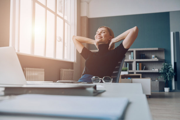 放松的女商人手握在脑后，微笑着坐在办公桌前图片下载