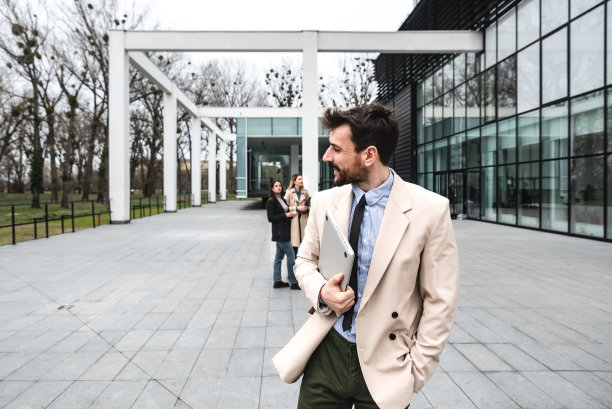 年轻的上班族，商务人士，在公司开完员工会议和演讲后，拿着笔记本电脑或平板电脑站在办公楼前，感到快乐、成功和自信图片下载