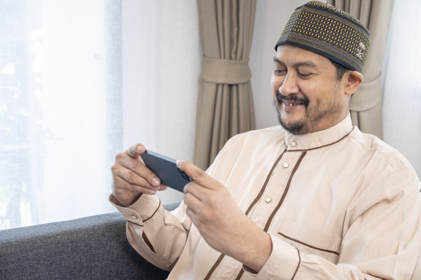 快乐的年轻亚洲穆斯林男子在家里使用手机图片下载