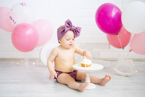 一个女婴在生日那天用粉红色的气球庆祝她的一岁，用手吃蛋糕，微笑着高兴图片下载