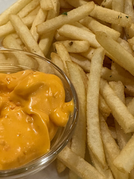 全画幅图片，一堆刚煮熟的，酥脆的，金黄色的炸薯条围绕着白色盘子上的蛋黄酱玻璃小蛋糕，高视图，重点在前景图片下载