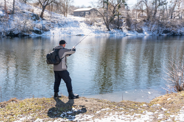 初春，一个渔夫背着背包，拿着鱼竿在白雪覆盖的河边捕鱼图片下载