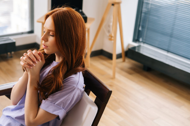 高角视角，焦虑的年轻女子闭着眼睛，双手合十，在家里的窗户前真诚地祈祷。图片下载