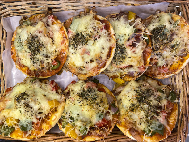 全画幅图片，一排排金色的，刚煮好的圆形迷你披萨，上面有红洋葱，灯笼椒，融化的切达奶酪，放在柳条篮子里，内衬有防水羊皮纸，高视图图片下载