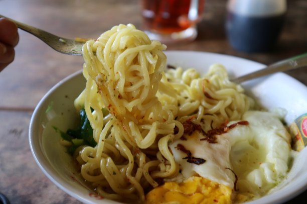 手用勺子和叉子拿食物的印米瓜或煮面条煮鸡蛋和绿芥末和在白色的碗。看起来又热又好吃。冰茶。图片下载