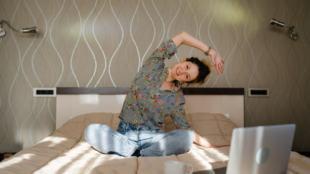 一名成年白人女性坐在酒店房间或家里的床上做瑜伽练习拉伸，每天早上例行复制空间图片下载