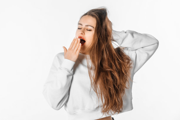 昏昏欲睡的年轻女子在打哈欠时捂着嘴。疲惫的黑发女性打哈欠无聊，对白色工作室背景摆姿势图片下载